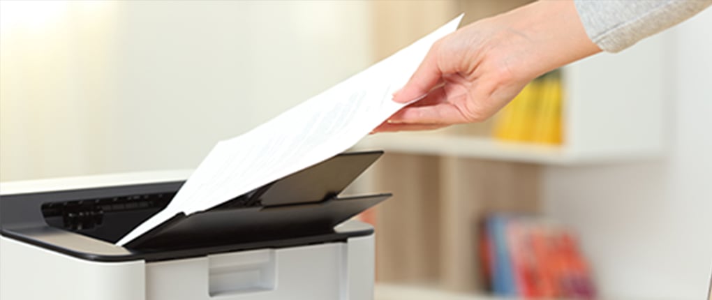 Image of a person holding a piece of paper and a printer