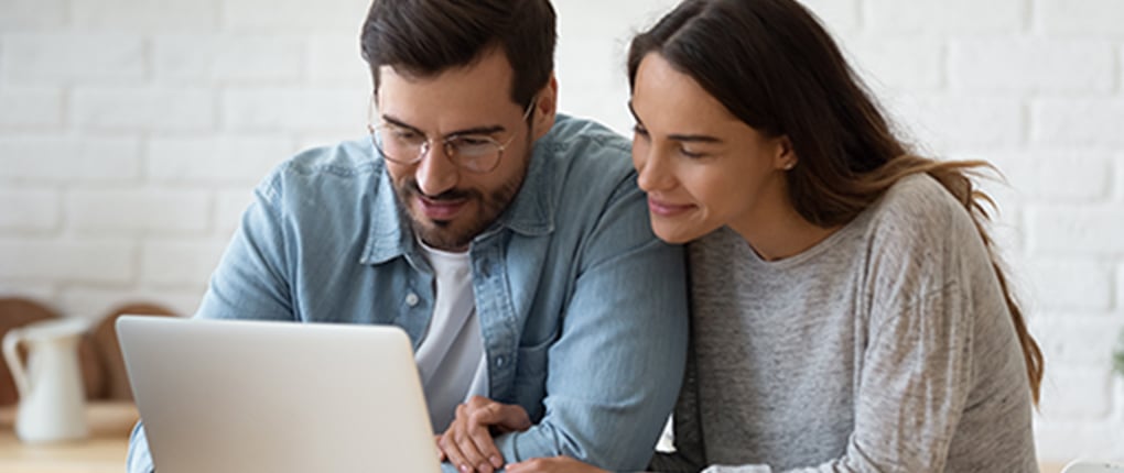 Image of a man and a woman sitting together and looking at a laptop screen.