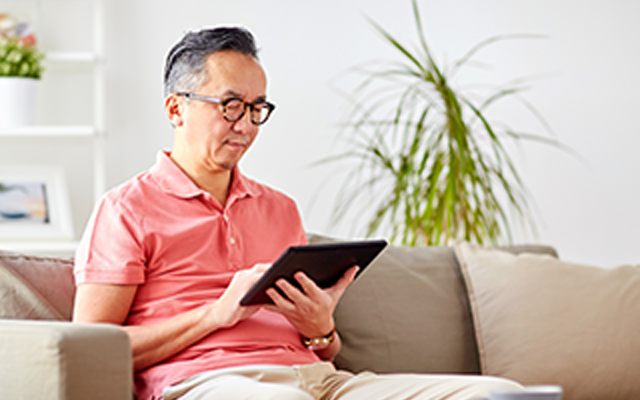 Image of a man sitting on a sofa using a tablet.