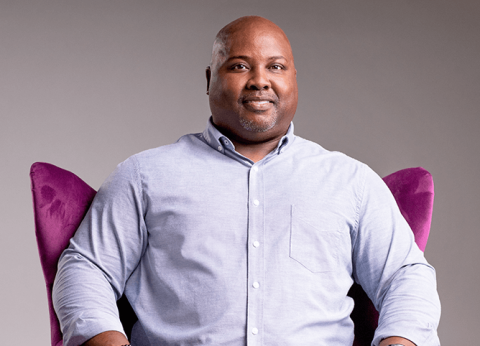 Image of a man in a light blue shirt sitting in a purple chair.