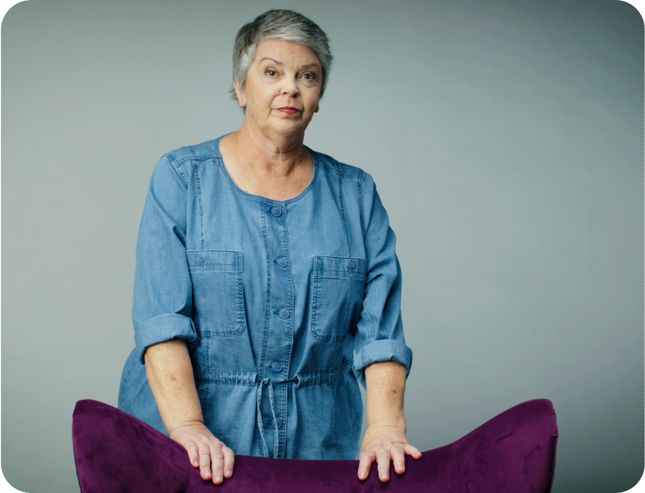 Image of a woman in a blue blouse standing behind a purple chair for The Purple Chair trailer.